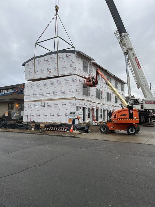 Crane lifting a modular unit with a scissor lift on site at a DanReDev development